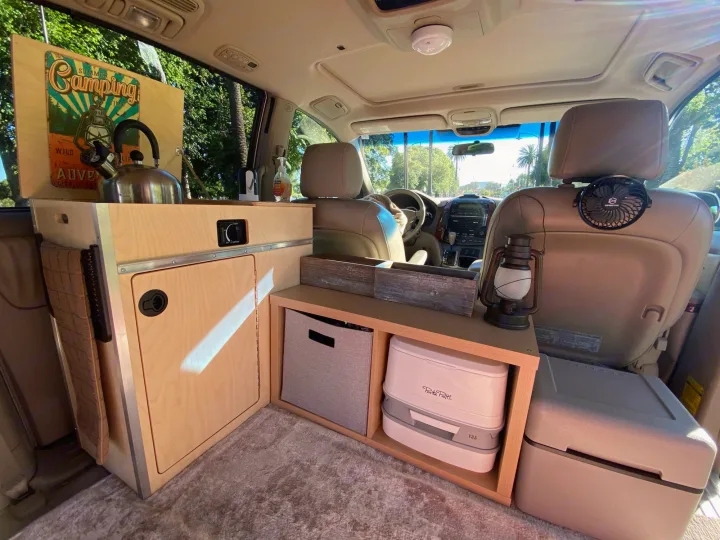 Inside a compact RV rental: custom wood setup with portable toilet, storage, and kettle for comfortable van life.. Custom Camper 2004