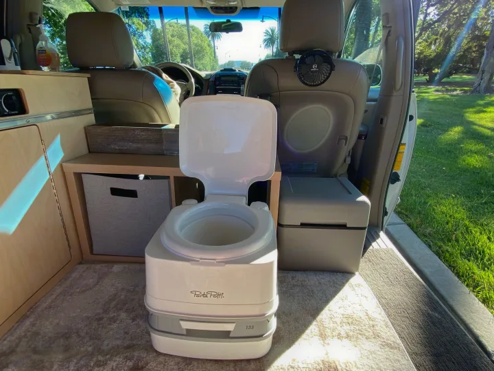 Inside this rv rental, a self-contained portable toilet sits on carpet, with built-in storage, and a fan for comfort.. Custom Camper 2004