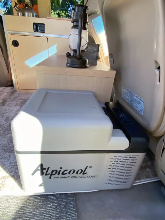 Interior of an RV rental, featuring an Alpicool portable fridge and custom wooden cabinetry for comfortable campervan travel.. Custom Camper 2004