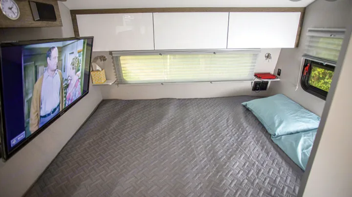 Compact RV rental interior featuring a comfortable bed with a quilted cover, wall-mounted TV, and smart storage solutions.. Intech Sol Horizon Rover 2022