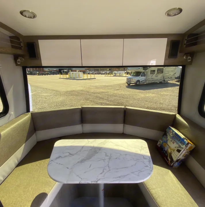 Inside an RV rental: Cozy dinette with marble table & U-shaped seating. View of RV lot outside.. Intech Sol Horizon Rover 2022