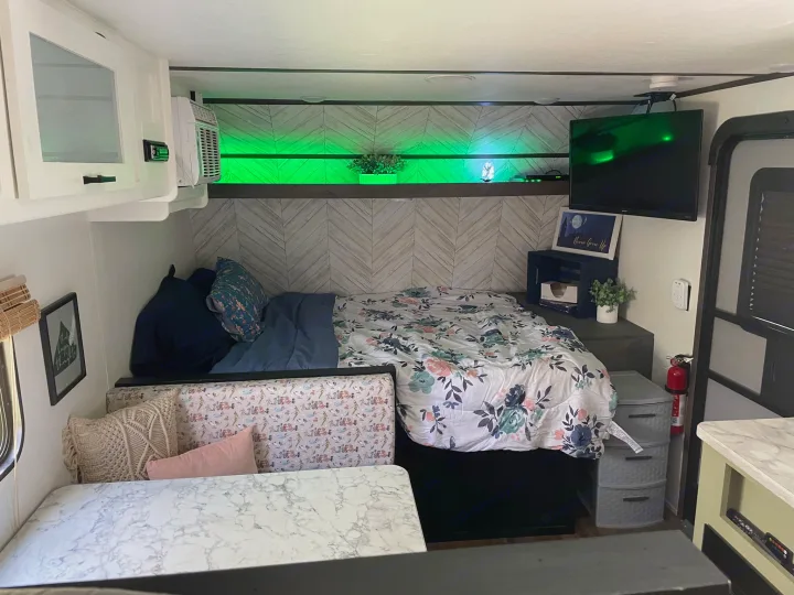 View of an RV rental's cozy interior, featuring a floral bed, dining area, TV, and decorative green lighting.. Dutchmen Coleman Lantern LT 2021