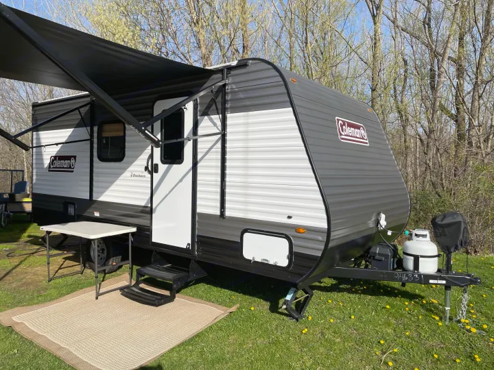 This Coleman travel trailer RV rental is set up with an awning, table, and rug for outdoor living.. Dutchmen Coleman Lantern LT 2021