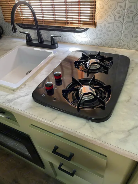 Modern RV rental kitchen with a sleek sink, two-burner cooktop, and stylish backsplash, perfect for mobile living.. Dutchmen Coleman Lantern LT 2021