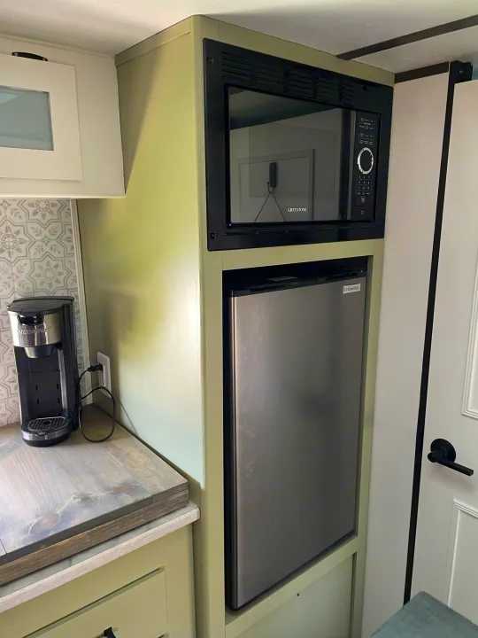 Compact rv rental kitchen features a Greystone microwave, Ever Chill mini-fridge, and coffee maker on light green cabinets.. Dutchmen Coleman Lantern LT 2021