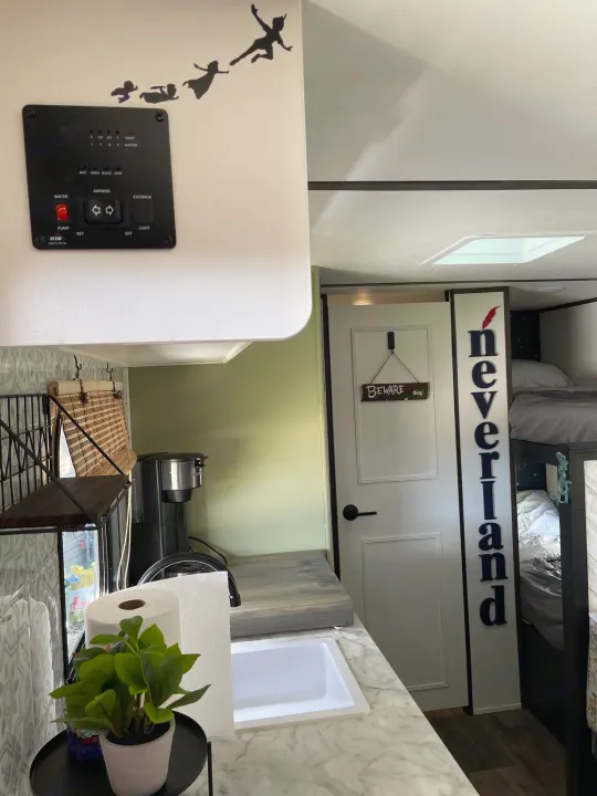 Peter Pan themed RV rental interior, featuring a kitchen area with control panel, sink, and bunk beds.. Dutchmen Coleman Lantern LT 2021