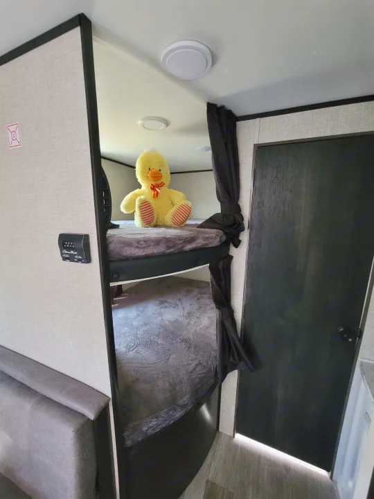 Cozy RV rental interior with bunk beds, a large yellow duck on the top bunk, a control panel, and a black door.. Jayco Jayco Jay Flight SLX 264bhw 2022