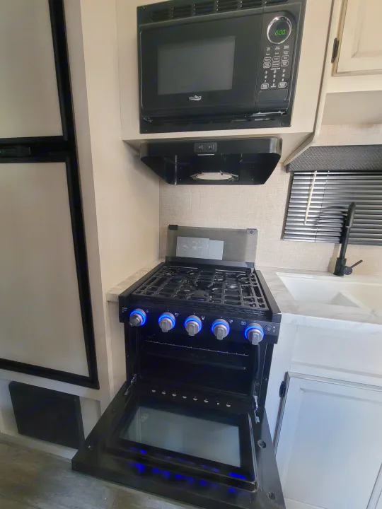RV rental kitchen showing a microwave, gas stove with lit knobs, open oven, sink, and part of a refrigerator.. Jayco Jayco Jay Flight SLX 264bhw 2022