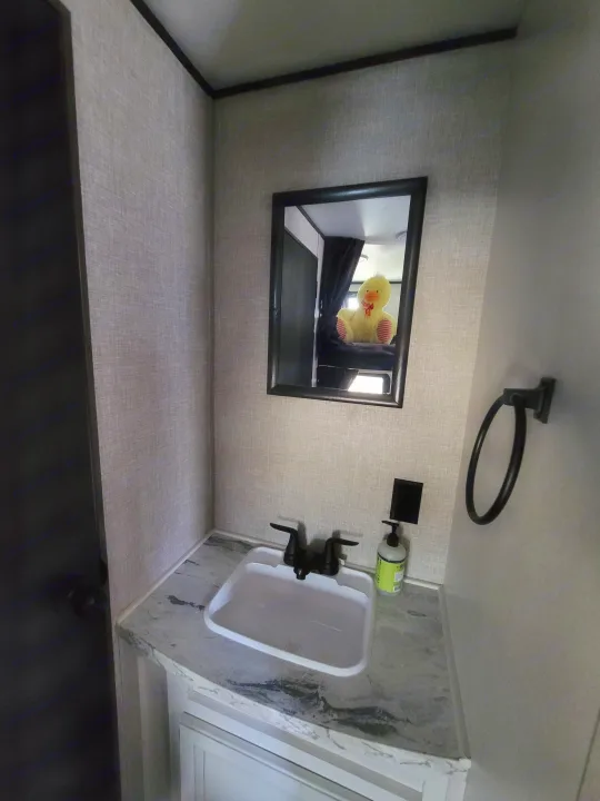 Compact RV rental bathroom with a white sink, dark fixtures, mirror reflecting a plush yellow duck, and textured gray walls.. Jayco Jayco Jay Flight SLX 264bhw 2022