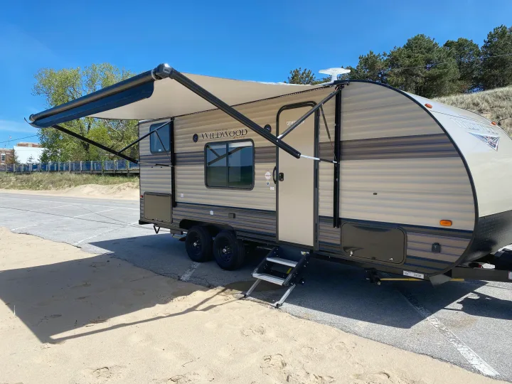 This RV rental, a Forest River Wildwood K-Lite, is parked on sand and asphalt with its awning out, ready for adventure.. Forest River Wildwood X-Lite 2019