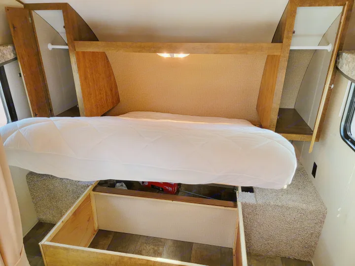 Inside an RV rental bedroom: quilted mattress lifted to reveal under-bed storage, flanked by built-in wardrobes and reading lights.. Crossroads RV Z-1 2015