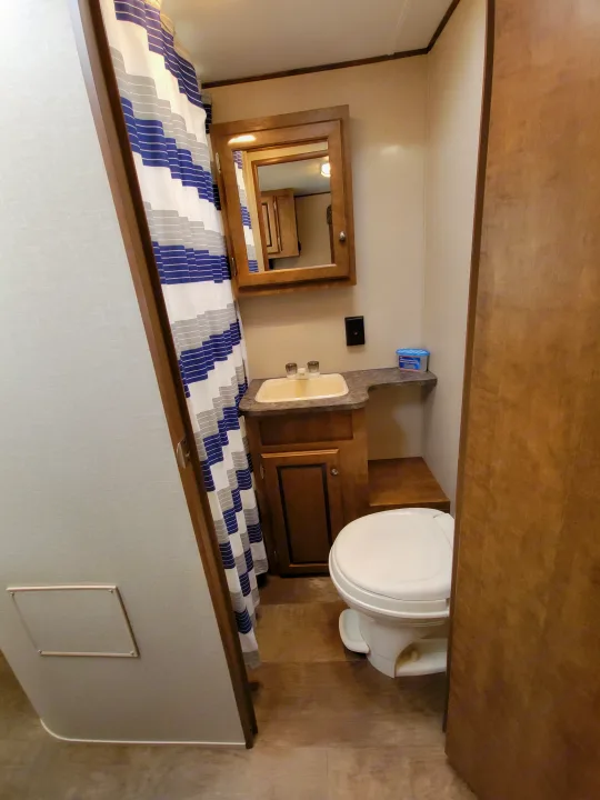 This RV rental's bathroom includes a toilet, a small vanity with a sink, a mirrored cabinet, and a blue/white striped shower.. Crossroads RV Z-1 2015