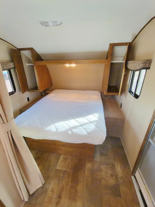 RV rental bedroom featuring a clean, white-covered bed, wooden shelving, and wood plank flooring, ready for guests.. Crossroads RV Z-1 2015