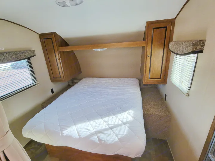 Clean RV rental bedroom featuring a white quilted bed, ample overhead storage, and window blinds.. Crossroads RV Z-1 2015