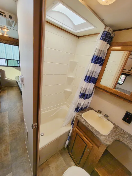 RV rental bathroom features a compact shower with skylight & striped curtain, sink, mirror, and toilet area.. Crossroads RV Z-1 2015