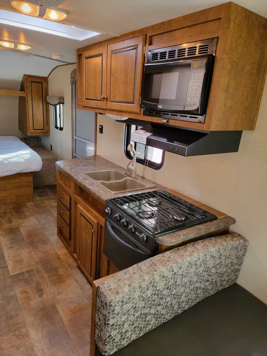 An RV rental's kitchen and dining space, showing microwave, stove, sink, cabinets, and a dinette with patterned cushions.. Crossroads RV Z-1 2015