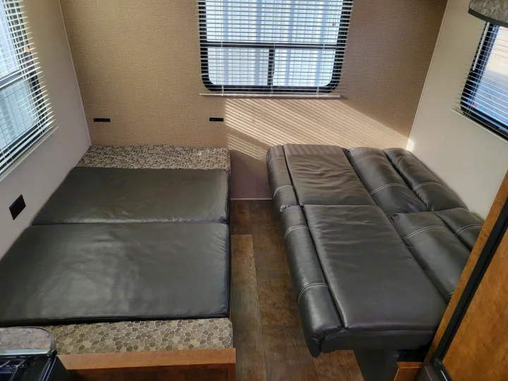 RV rental interior: Comfortable living area with a dark leather convertible sofa and dinette bed, lit by window blinds.. Crossroads RV Z-1 2015