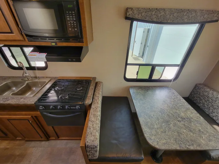 RV rental kitchen and dinette, featuring a microwave, gas stove, double sink, and comfortable booth seating.. Crossroads RV Z-1 2015