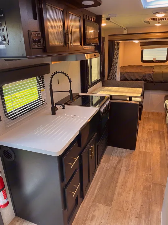 Modern RV rental interior with a sleek kitchen (white counter, black fixtures), cozy dinette, and comfortable bedroom, ideal for travel.. Forest River Cherokee Grey Wolf 2021