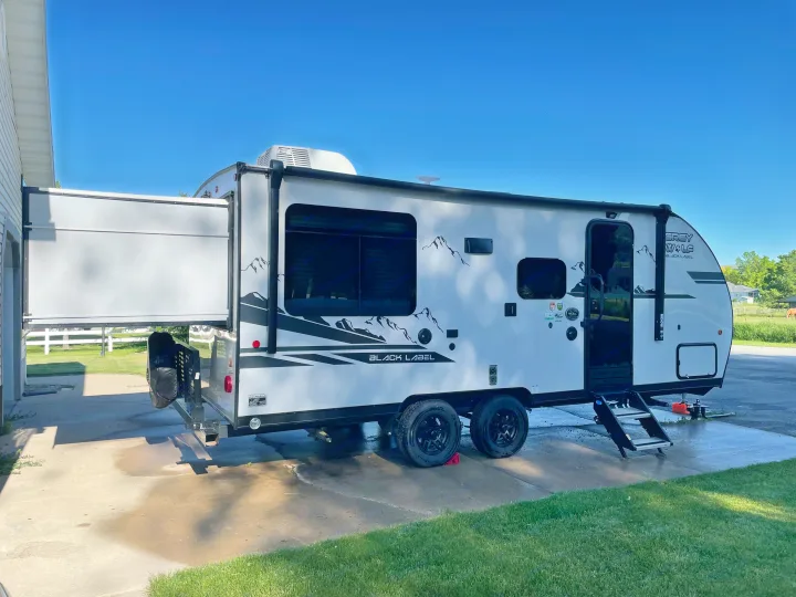 White Grey Wolf travel trailer with rear ramp open, possibly for an RV rental, being washed on a driveway.. Forest River Cherokee Grey Wolf 2021