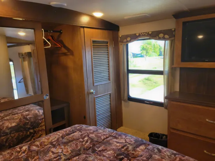 Cozy RV rental bedroom featuring a bed, mirrored closet, window, and entertainment area with a TV.. Keystone Montana 2017