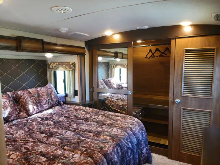 RV rental bedroom: a bed with camo bedding, diamond-stitched headboard, and reflective wardrobe door.. Keystone Montana 2017