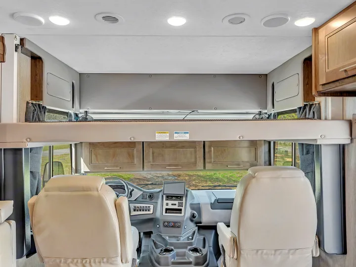 Step into this RV rental, showcasing its driver's cab, overhead bunk, and inviting interior for comfortable travel.. Coachmen Mirada 2021