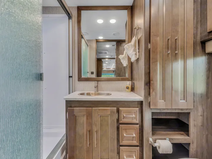 RV rental bathroom with light wood vanity, sink, mirror, shower, cabinets & toilet paper holder.. Coachmen Mirada 2021