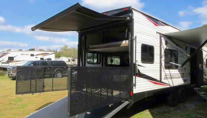 This white toy hauler RV rental features extended awnings and a rear patio with mesh enclosure. Bunk beds are visible inside this camper.. Forest River Shockwave 2022