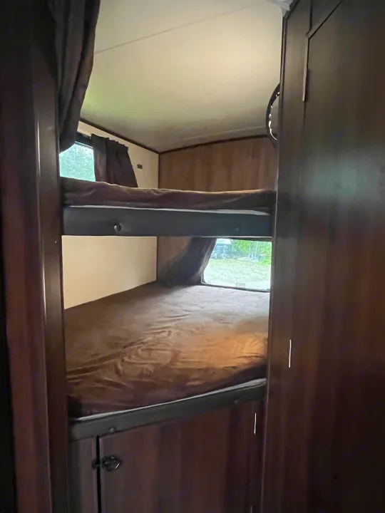 Inside an RV rental, upper and lower bunk beds create a compact sleeping space with a window view.. Jayco White Hawk 2018