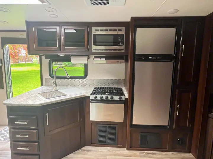 Inside an RV rental: a modern kitchen with dark wood cabinets, sink, stove, microwave, and fridge, ready for your adventures.. Jayco White Hawk 2018