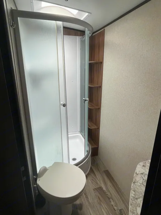 Inside an RV rental: a clean bathroom with a glass shower, white toilet, and practical overhead storage.. Jayco White Hawk 2018
