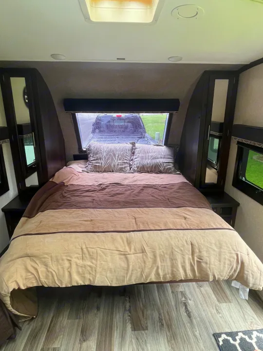 Cozy RV rental bedroom interior with a comfortable striped bed, patterned pillows, and a window view of a truck outside.. Jayco White Hawk 2018