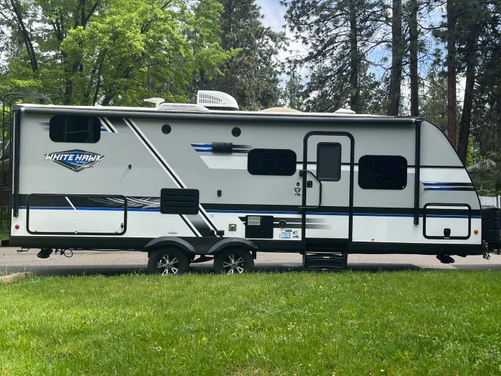 A sleek, modern White Hawk travel trailer (RV rental) in grey and white, parked on a grassy patch.. Jayco White Hawk 2018