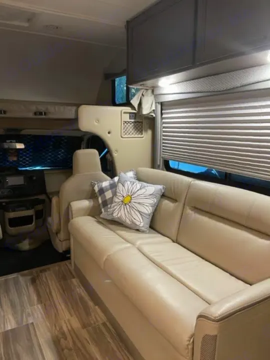 Inviting RV rental interior: cream leather sofa with plaid/daisy pillows, wood floors, and modern overhead storage. Ready for road trips!. Thor Four Winds 2022