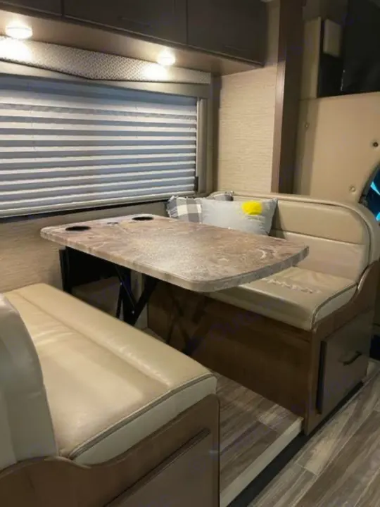This RV rental features a comfortable dinette area with a table and bench seating, perfect for meals on the road.. Thor Four Winds 2022
