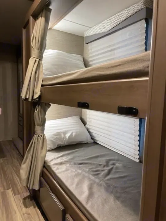 Compact RV rental bunk beds with pillows, sheets, and privacy curtains, ideal for family travel.. Thor Four Winds 2022