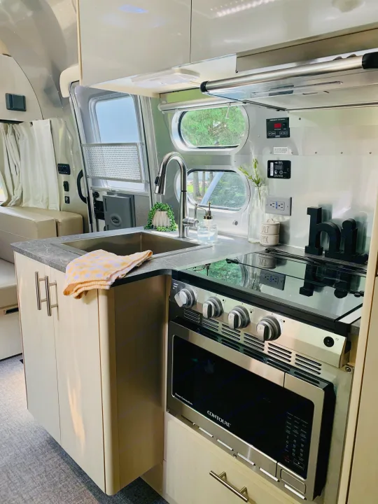 A bright and modern RV rental kitchen with a stainless steel sink, stove, oven, and ample storage cabinets.. Airstream Flying Cloud 2022