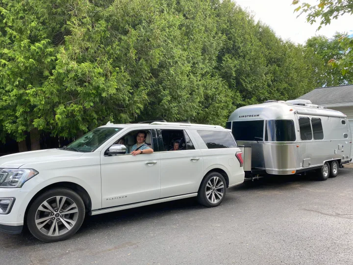 Smiling family in a Ford Expedition towing an Airstream rv rental, setting off for a camping road trip adventure!. Airstream Flying Cloud 2022
