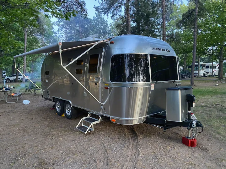Airstream travel trailer **RV rental** set up in a wooded campsite with an extended awning and picnic area.. Airstream Flying Cloud 2022