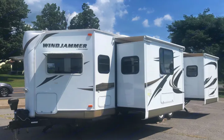 White Windjammer RV rental with multiple slide-outs extended, parked outdoors on asphalt under a sunny sky.. Forest River Rockwood Windjammer 2012