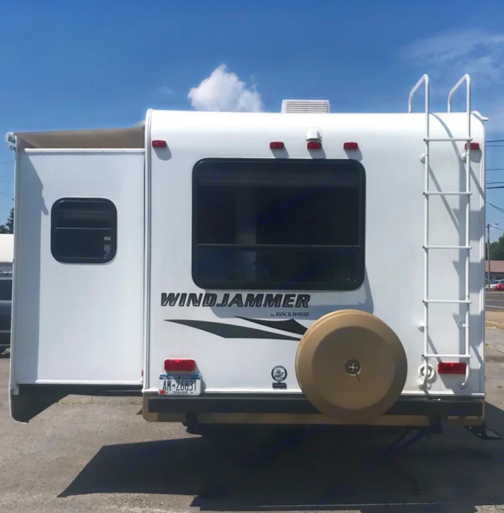 White Windjammer travel trailer's rear. Features a slide-out, ladder, and spare tire, ready for an RV rental adventure.. Forest River Rockwood Windjammer 2012