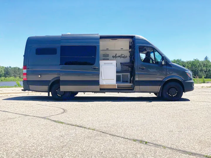Stylish gray camper van, an ideal rv rental, parked outdoors with its side door open revealing a custom "adventure" interior.. Mercedes-Benz Sprinter 2015