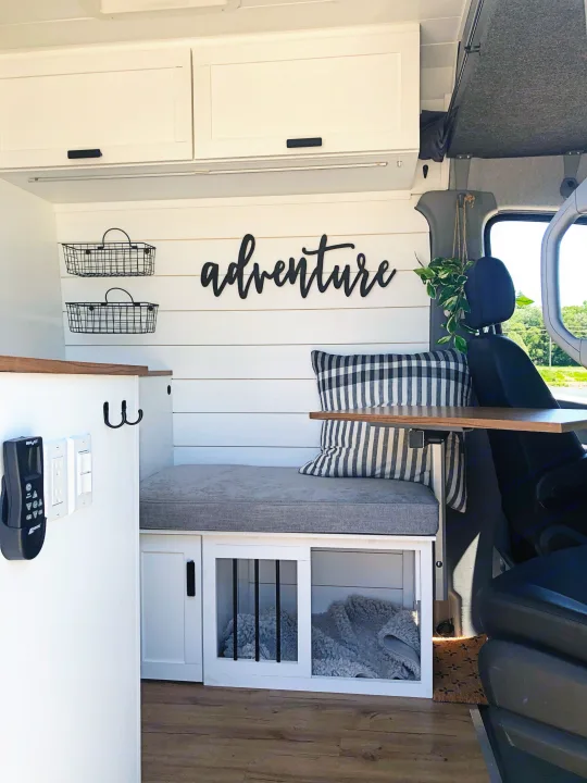 Modern rv rental van interior: 'adventure' sign, white shiplap walls, cozy bench with dog bed, cabinets, and storage.. Mercedes-Benz Sprinter 2015