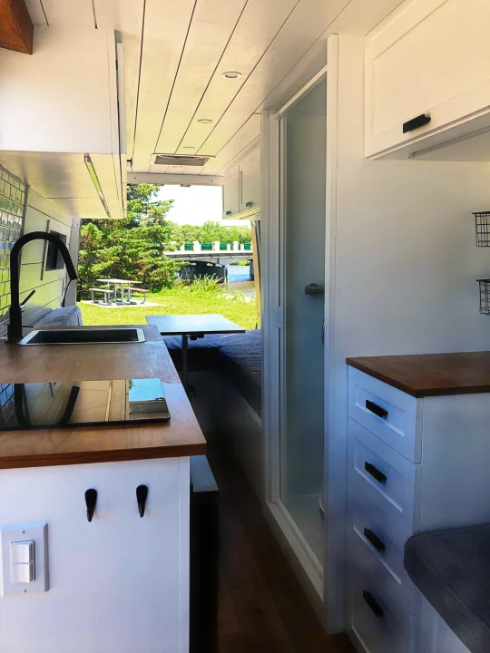 Inside a modern RV rental: well-equipped kitchen, compact shower, and panoramic outdoor views. Perfect for travel adventures.. Mercedes-Benz Sprinter 2015