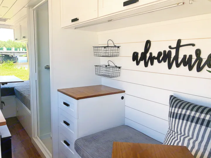 RV rental interior: bright, modern design with custom cabinets, cozy seating, shower, and "adventure" sign for travel comfort.. Mercedes-Benz Sprinter 2015