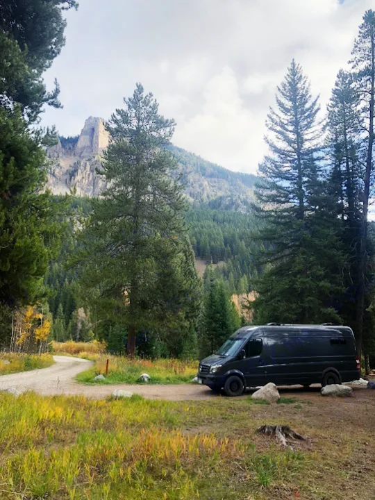 Adventure awaits! An RV rental camper van nestled among fall trees with a majestic mountain background. Perfect for road trips.. Mercedes-Benz Sprinter 2015