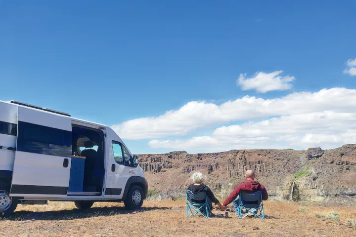 A couple by their RV rental enjoys stunning canyon views with a waterfall. Ideal for adventurous road trips.. Dodge Promaster 2500 2021