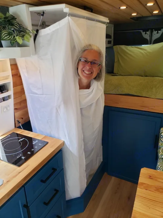A woman smiles from her custom van's clever pop-up shower, showcasing the compact kitchenette in this rv rental.. Dodge Promaster 2500 2021
