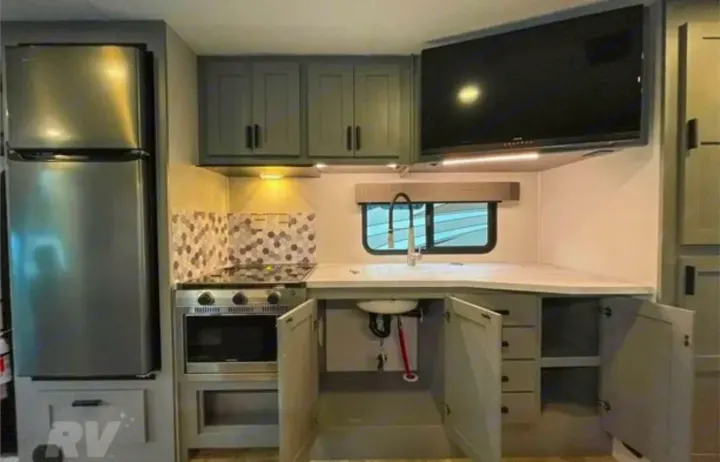 Inside a modern **rv rental**: a compact kitchen with stainless appliances, grey cabinetry, and a wall-mounted TV.. Forest River Solera 2022